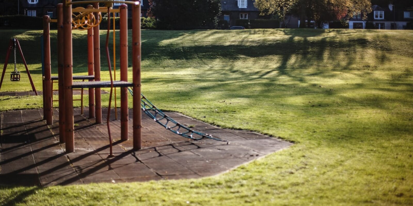 Wooden climbing frame on a playground surface beside an open lawn